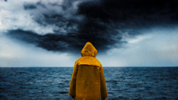 A person wearing a yellow rain jacket looks out at the ocean during a rainstorm.