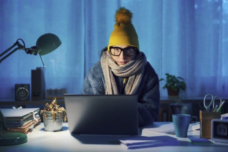 A woman works from home at her computer while wearing winter close.