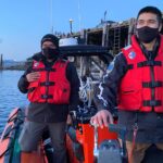 Two Coastal Nations Coast Guard Auxiliary members with life jackets on a boat.